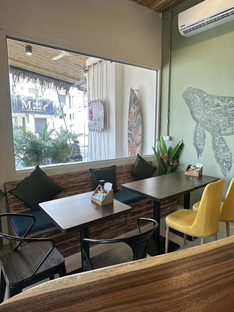 Interior seating area showing the relaxed vibe at Wilson’s Cafe Phuket Town with wooden tables and window view